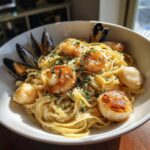 Close-up of a creamy seafood pasta dish featuring seared shrimp, scallops, and mussels, garnished with parsley.