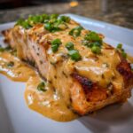 Close-up of a perfectly cooked piece of bang bang salmon smothered in creamy orange sauce and topped with green onions.
