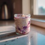 A single serving of blueberry overnight oats layered in a glass mason jar, sitting on a countertop in warm morning sunlight.