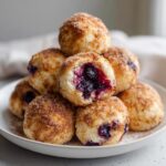 A stack of warm Blueberry Pie Bombs dusted with cinnamon sugar, one cut open showing the rich blueberry filling.