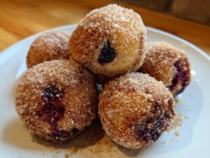 A close-up of five golden-brown Blueberry Pie Bombs coated in cinnamon sugar on a white plate.