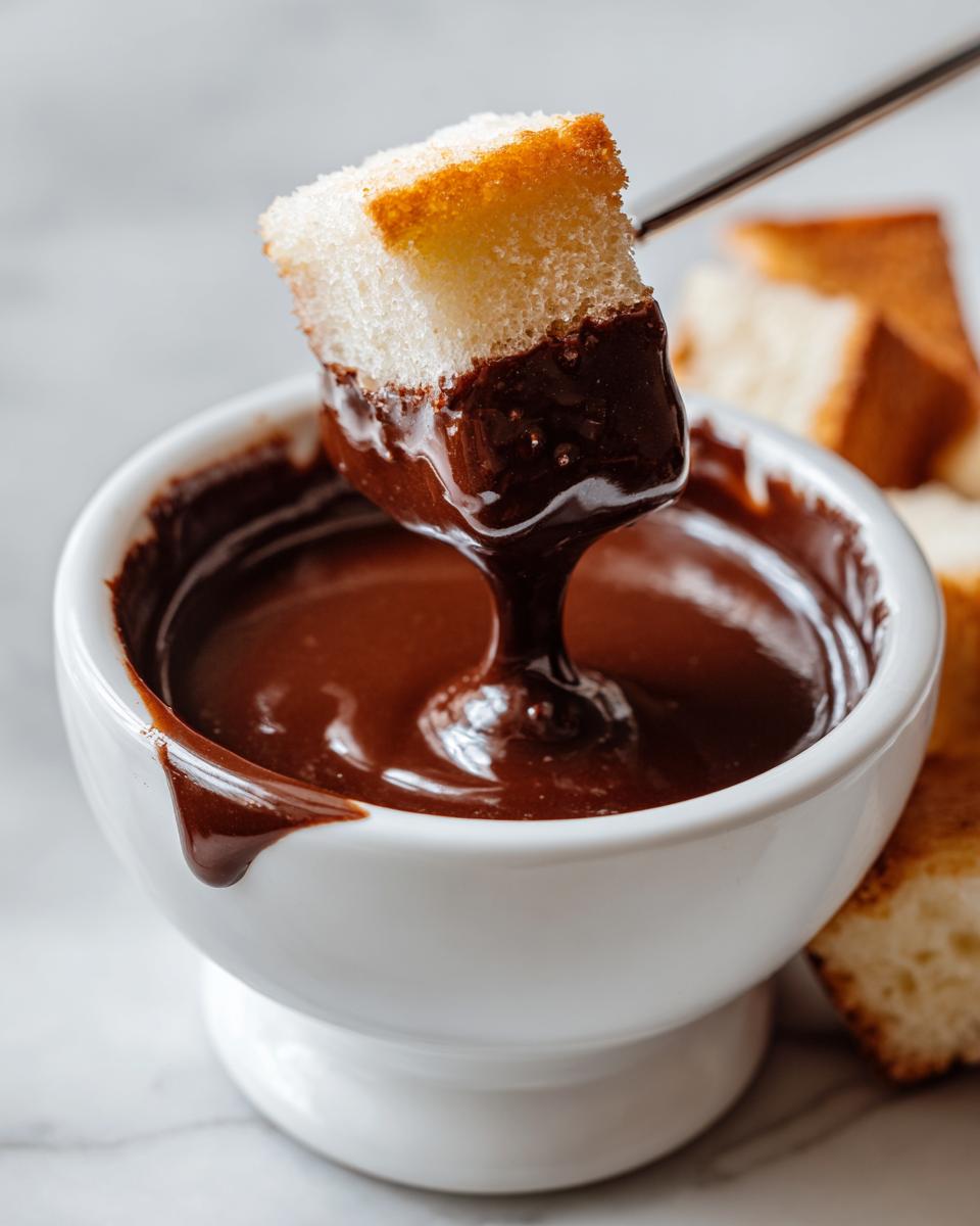 A piece of pound cake being dipped into rich, melted chocolate fondue in a white bowl.