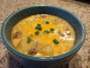 A close-up of a hearty serving of cheeseburger soup recipe, topped with melted cheddar cheese and chopped green onions.