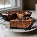 A thick slice of decadent chocolate mousse pie with a dark crust, topped with chocolate shavings.
