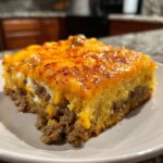 A close-up slice of cowboy cornbread casserole with a cheesy, browned top layer over seasoned ground beef.