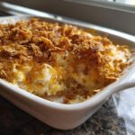 A close-up view of a creamy baked potato casserole in a white dish, featuring melted cheese and a golden, crunchy topping.