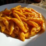 Close-up of penne pasta coated in a rich, orange, creamy butternut squash pasta sauce on a white plate.