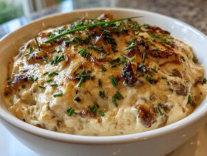 Close-up of a bowl filled with creamy caramelized onion dip, topped with browned onions and fresh green chives.