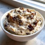 Close-up of a creamy onion dip topped with caramelized onions served in a white bowl near a window.