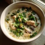 Close-up of a creamy chicken and mushroom coconut soup garnished heavily with fresh cilantro.