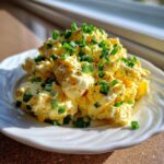 A mound of creamy, yellow egg salad recipe garnished generously with chopped green chives and black pepper.