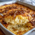 A spoonful of creamy french onion butter rice lifted from a baking dish, topped with caramelized onions.