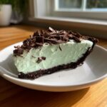A close-up slice of creamy, light green grasshopper pie with a dark chocolate crust, topped with chocolate shavings.