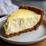 A thick slice of creamy lemon pie with a graham cracker crust, topped with bright yellow lemon zest.