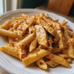 A close-up of creamy marry me chicken pasta featuring penne noodles and sliced chicken breast on a white plate.