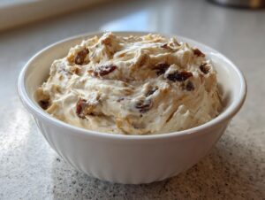 A close-up of creamy onion dip mixed with dark, caramelized onions served in a white bowl.