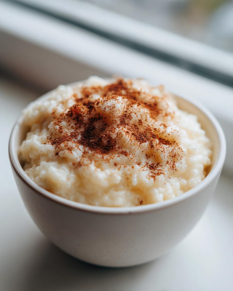 Close-up of creamy rice pudding topped generously with ground cinnamon in a white bowl.