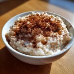 Close-up of a white bowl filled with creamy rice pudding recipe, generously sprinkled with ground cinnamon.