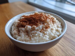 A close-up of creamy rice pudding recipe served in a white bowl, generously dusted with ground cinnamon.