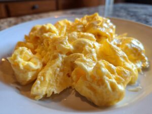 Close-up of fluffy, creamy scrambled eggs served on a white plate, showcasing the rich yellow color.