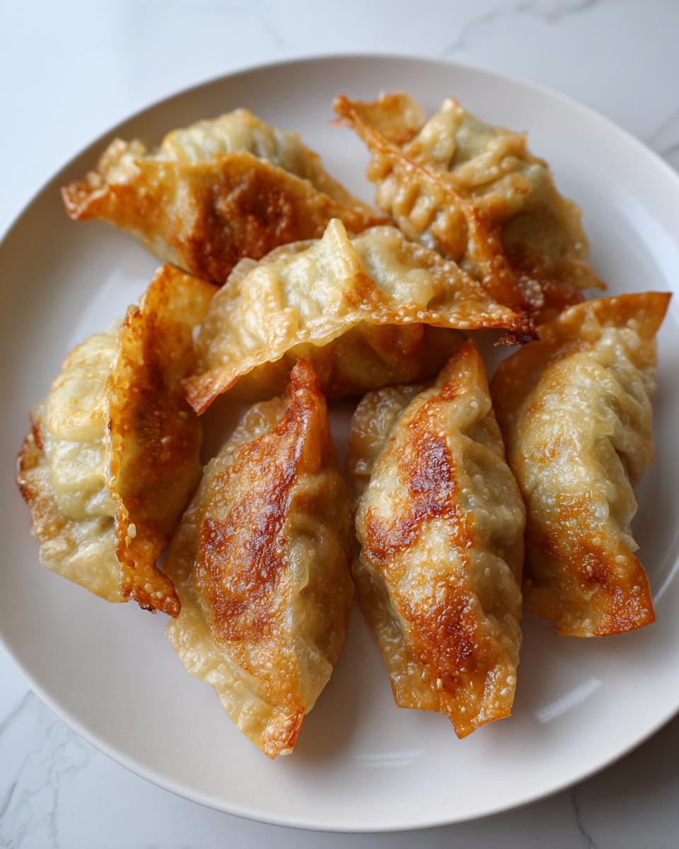 A close-up of several golden-brown, crispy pan-fried rice paper dumplings arranged on a white plate.