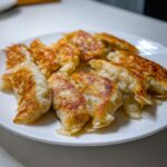 Close-up of several golden-brown, pan-fried rice paper dumplings arranged on a white plate.