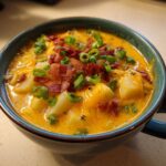 A close-up of creamy crockpot cheeseburger soup filled with potatoes, melted cheddar cheese, crispy bacon bits, and fresh green onions.