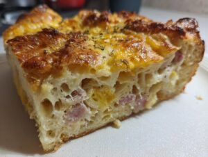 Close-up of a thick slice of Croissant Breakfast Casserole showing flaky bread, melted cheese, and pieces of ham.