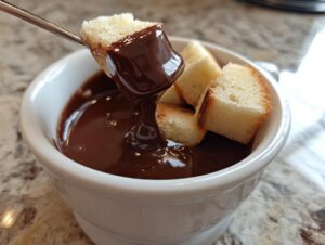 A piece of pound cake is dipped into rich, melted chocolate fondue using a fondue fork.