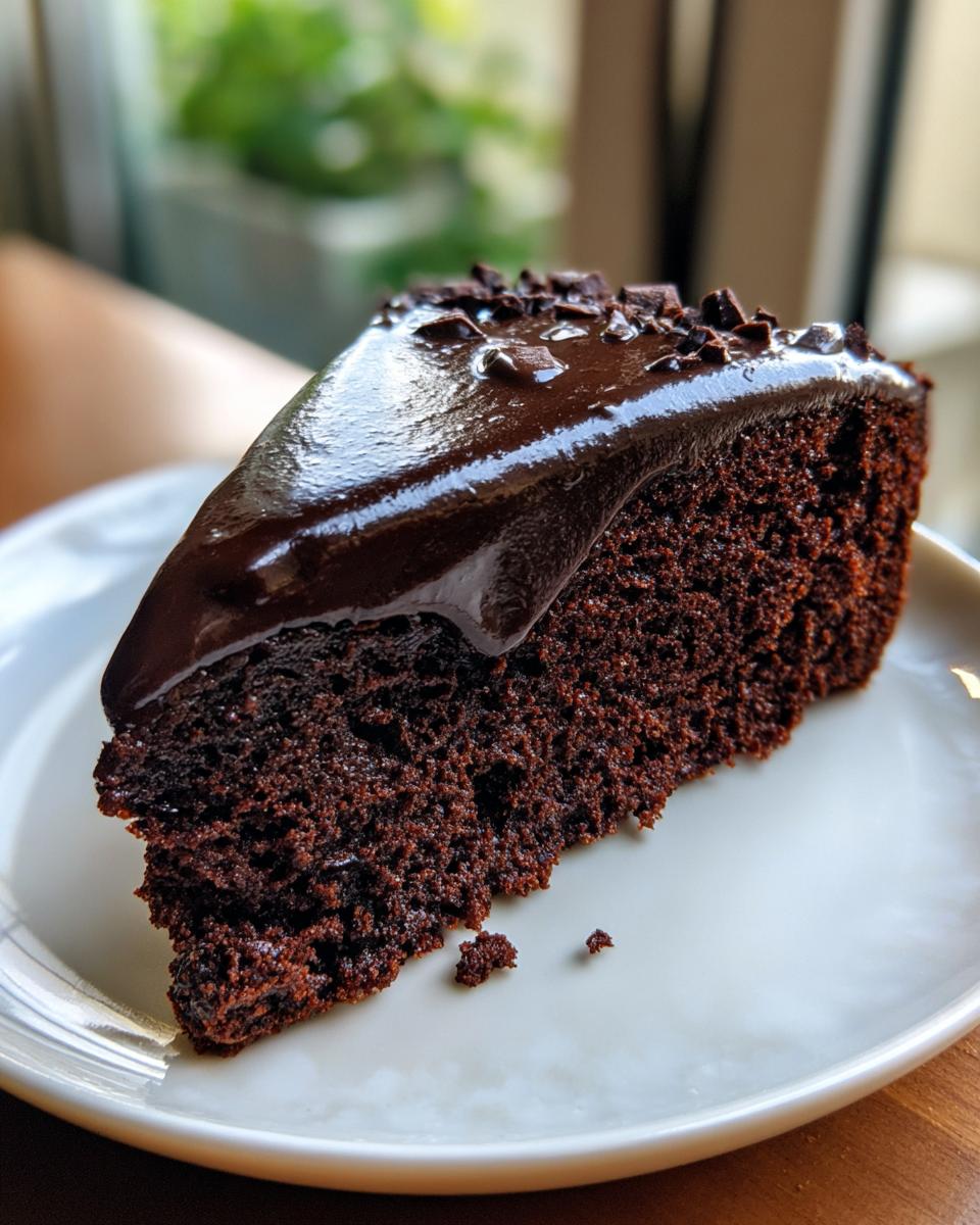 A close-up of a moist slice of flourless chocolate cake topped with shiny chocolate ganache and sprinkles.