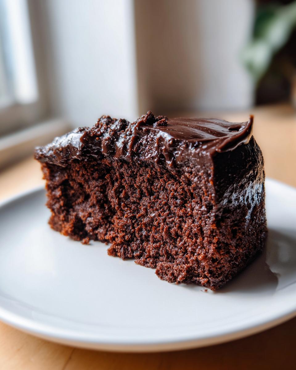 A close-up of a moist slice of flourless chocolate cake topped with glossy chocolate frosting.