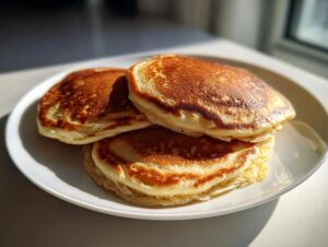 A stack of three fluffy banana oatmeal pancakes with golden-brown tops served on a white plate.