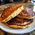 Close-up of a stack of golden brown oatmeal pancakes, one cut to show the fluffy, airy interior texture.