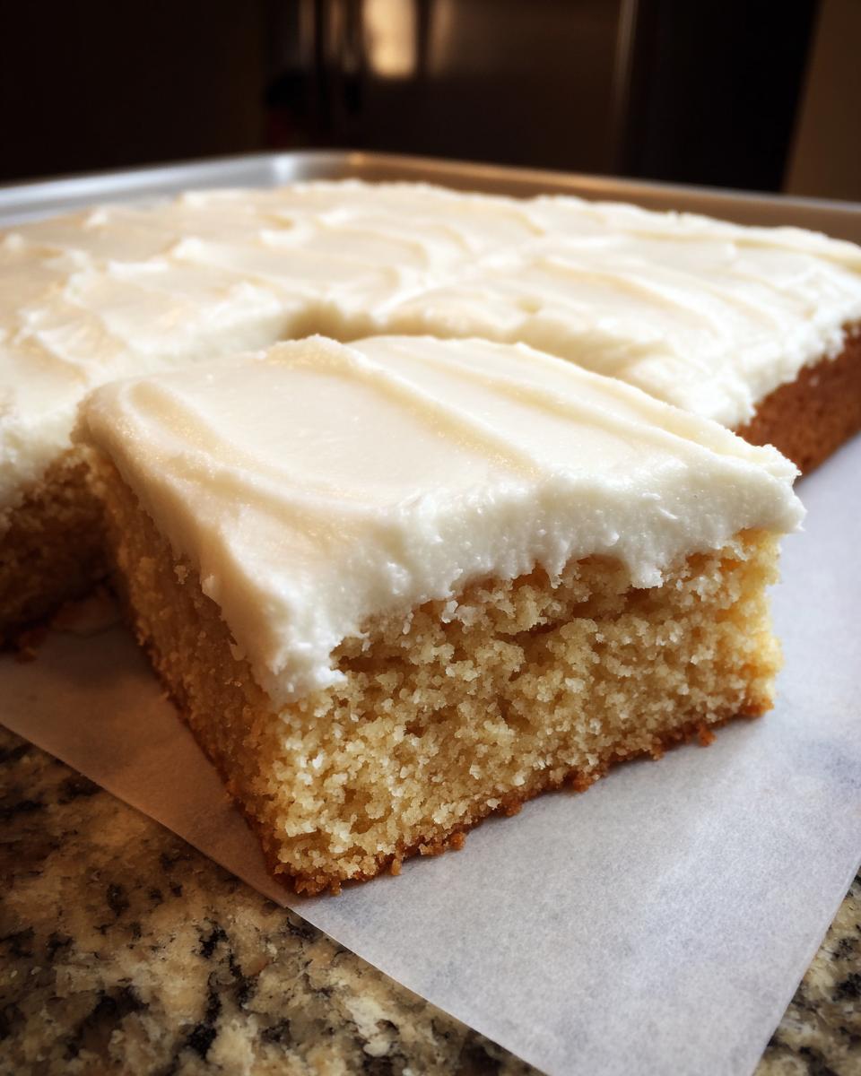 A thick, square slice of moist sugar cookie bars topped with creamy white frosting, sitting next to the rest of the pan.