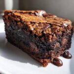 Close-up of a single, fudgy brownies square showing a shiny, cracked top and melted chocolate chips.