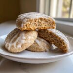 A stack of soft, spiced persimmon cookies drizzled with white glaze, one cookie is broken open.