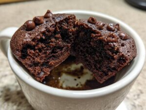 Close-up of a rich, dark chocolate mug cake cut in half inside a white mug, showing its moist texture and chocolate chips.