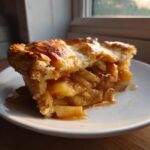 A close-up of a delicious slice of homemade apple pie showing thick apple filling and a golden, flaky crust.