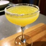 A vibrant yellow lemon drop martini served in a coupe glass with a thick, sparkling sugar rim.