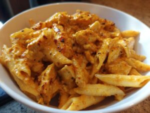 Close-up of a white bowl filled with creamy marry me chicken pasta featuring penne noodles and rich orange sauce.