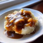 A serving of fluffy mashed potatoes generously topped with rich, glossy homemade brown gravy.