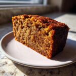 A close-up, sunlit slice of moist, dark brown applesauce cake on a small plate.