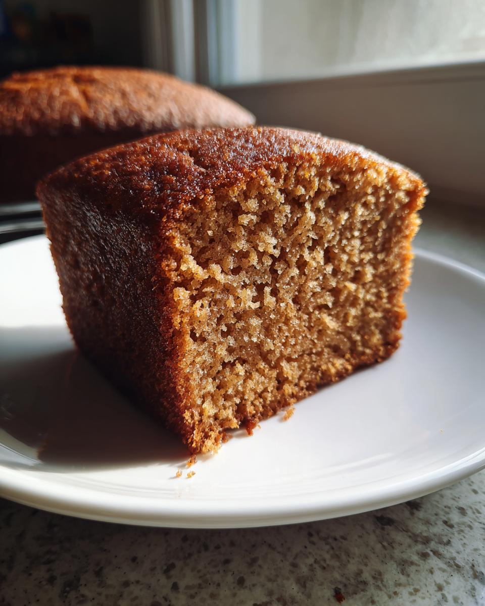 Close-up of a moist, square slice of brown applesauce cake showing its fine, tender crumb texture on a white plate.