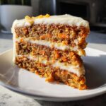 Close-up of a tall, moist slice of carrot cake recipe with thick cream cheese frosting layers.