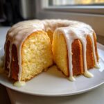 A slice cut from a bundt-shaped lemon pound cake covered in thick white glaze.