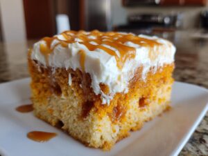 A close-up of a moist slice of pumpkin poke cake topped with whipped cream and caramel sauce.