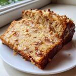 Two moist slices of hawaiian banana bread topped with caramelized fruit and chopped nuts on a white plate.