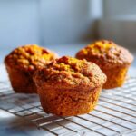 Three freshly baked sweet potato muffins with a rich orange color cooling on a wire rack.