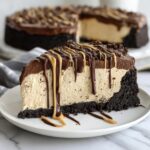 A decadent slice of no bake peanut butter pie featuring a dark crust, creamy filling, and chocolate ganache topped with peanut butter drizzle.