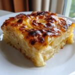 A square slice of creamy potatoes au gratin with a deeply browned, bubbly cheese crust on a white plate.